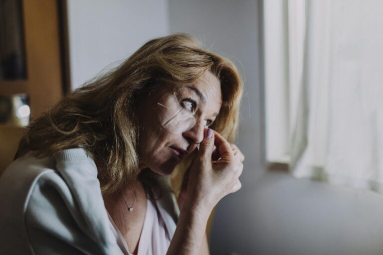 A woman applies an eye patch symbolizing self-care and relaxation indoors.